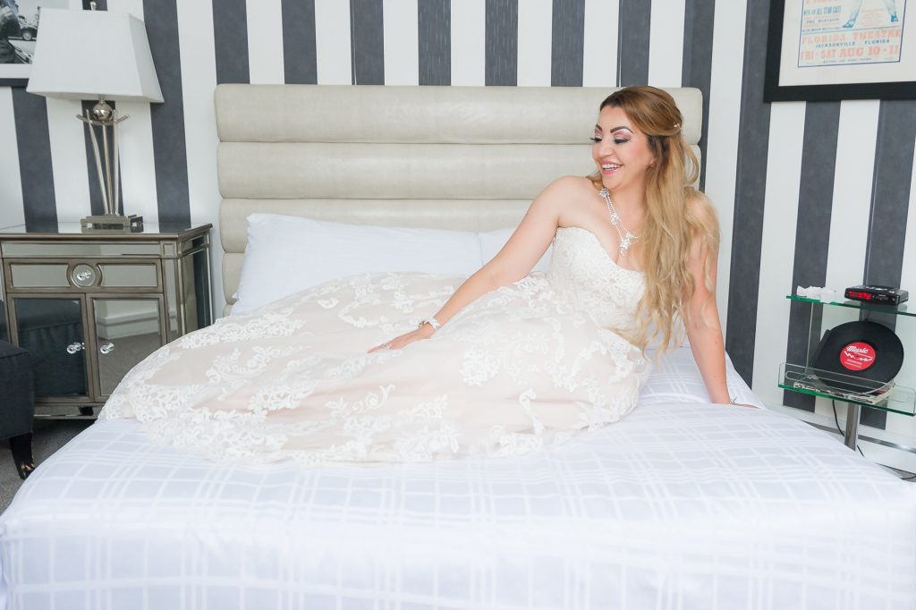 bride enjoying herself, sitting on a bed in her beautiful wedding dress in Chatham